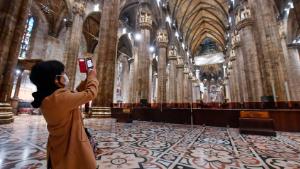 FILE - In this Monday, March 2, 2020 file photo, a tourist wearing a face mask takes pictures inside the Duomo gothic cathedral as it reopened to the public after being closed due to the COVID-19 virus outbreak in northern Italy,  in Milan. The focal point of the coronavirus emergency in Europe, Italy, is also the region's weakest economy and is taking an almighty hit as foreigners stop visiting its cultural treasures or buying its prized artisanal products, from fashion to food to design. Europe's third-largest economy has long been among the slowest growing in the region and is the one that is tallying the largest number of virus infections outside Asia. (Claudio Furlan/LaPresse via AP, File)