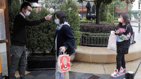 A staff member checks the body temperature of visitors outside Disneytown in Shanghai on Monday.