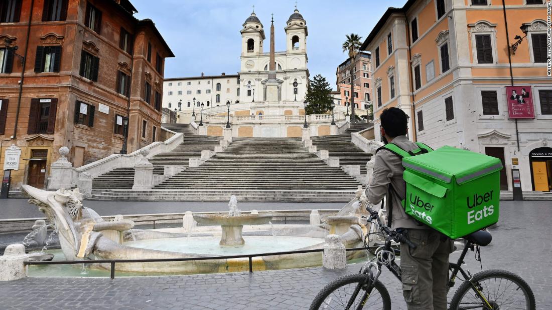 An Uber Eats delivery biker stands at a deserted Piazza di Spagna in Rome.