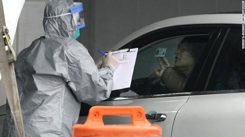 Workers in protective suits check IDs as people arrive to be tested for coronavirus at a drive-up testing facility in Glen Island Park in New Rochelle, New York, on March 13, 2020.