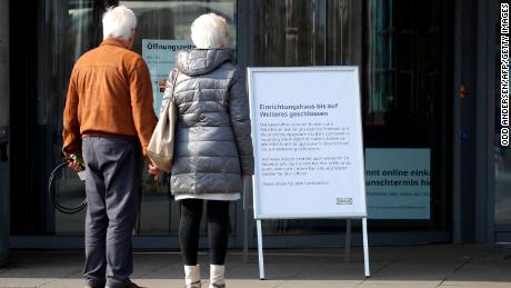 A couple stands in front of a sign that says a store is closed in Germany.