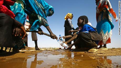  A Sudanese woman fills water bottles held by a young boy near the capital of the North Darfur State. 