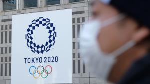 A man wearing a mask passes the logo of the Tokyo 2020 Olympic Games displayed on the Tokyo Metropolitan Government building on March 19, 2020. (Photo by Kazuhiro NOGI / AFP) (Photo by KAZUHIRO NOGI/AFP via Getty Images)