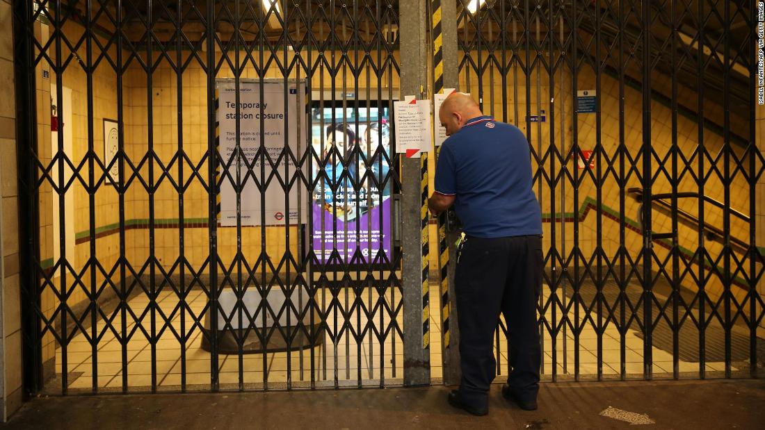 A worker closes the gates at Barbican Underground station as public transport services in London are reduced.