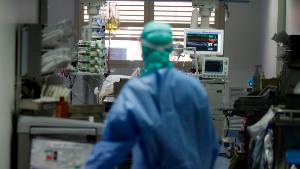 In this March 16, 2020, photo, a doctor watches a coronavirus patient under treatment in the intensive care unit of the Brescia hospital, Italy. Hospitals in northern Italy are struggling to make room for the onslaught of coronavirus patients. (AP Photo/Luca Bruno)