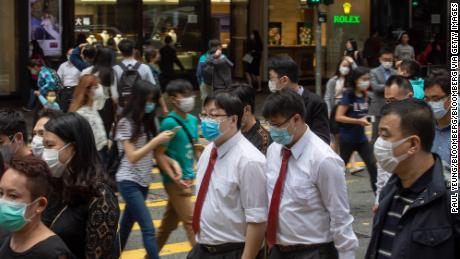 Office workers and pedestrians wearing protective masks walk along Queen&#39;s Road Central in the Central district of Hong Kong on Friday, March 20, 2020.