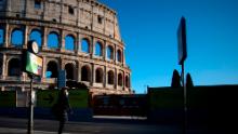 A woman wearing a protective mask waits at a bus stop near the Colosseum monument along a deserted Via dei Fori Imperiali on March 23, 2020 in Rome, during the country&#39;s lockdown aimed at stopping the spread of the COVID-19 (new coronavirus) pandemic. (Photo by Filippo MONTEFORTE / AFP) (Photo by FILIPPO MONTEFORTE/AFP via Getty Images)