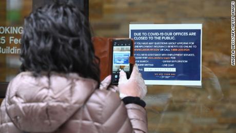 A woman takes a picture of a sign in front of the closed Department of Labor on March 25, 2020 in New York. - Wall Street stocks jumped early Wednesday as markets awaited a vote on a $2 trillion package agreed by congressional leaders to boost the US economy ravaged by the coronavirus outbreak. (Photo by Angela Weiss/AFP/Getty Images)