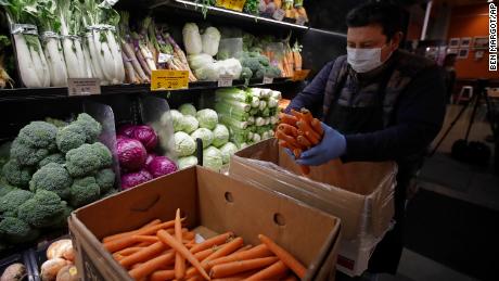 A worker, wearing a protective mask against the coronavirus, stocks produce at Gus&#39;s Community Market in San Francisco. 