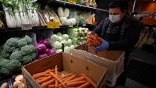 A worker, wearing a protective mask against the coronavirus, stocks produce at Gus&#39;s Community Market in San Francisco. 