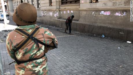 A soldier looks on past a man on crutches during South Africa&#39;s lockdown.