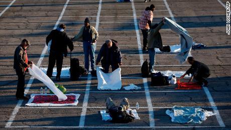 People prepare places to sleep in area marked by painted boxes on the ground of a parking lot at a makeshift camp for the homeless Monday, March 30, 2020, in Las Vegas. 