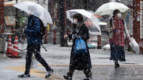 Snow falls as people wearing face masks walk through Tokyo&#39;s  Asakusa district on March 29.