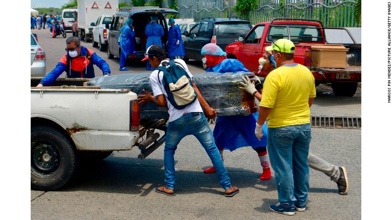 Men with protective suits load a coffin into a car in front of a Guayaquil hospital.