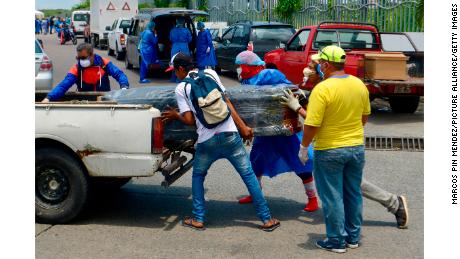 Bărbații care au echipament de protecție încarcă un sicriu într-o mașină din fața unui spital din Guayaquil.