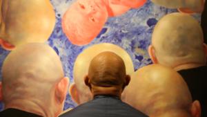 Chinese artist Fang Lijun pictured with one of his paintings, which since the 1990s have often featured bald-headed protagonists. The artist uses the hairless figures as symbols of disillusionment and rebellion in modern China.