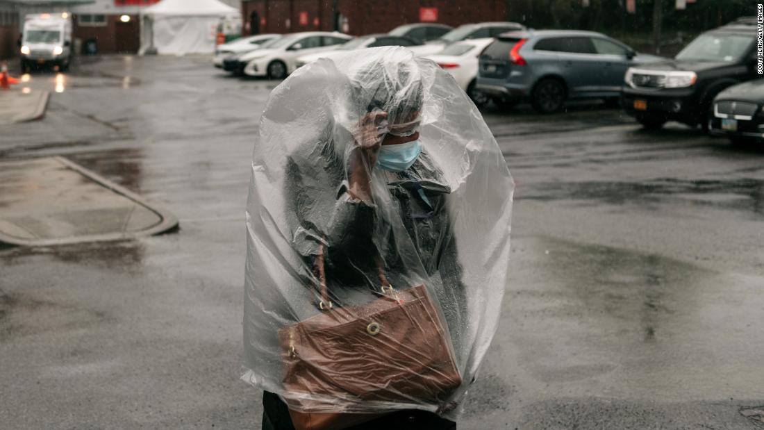 A woman covers herself with plastic as heavy rain falls outside a New York hospital on April 13, 2020.