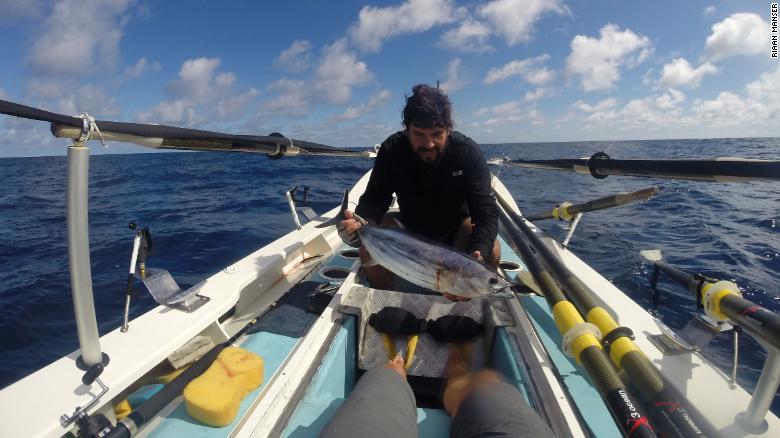 Riaan Manser holding a fish on his row boat