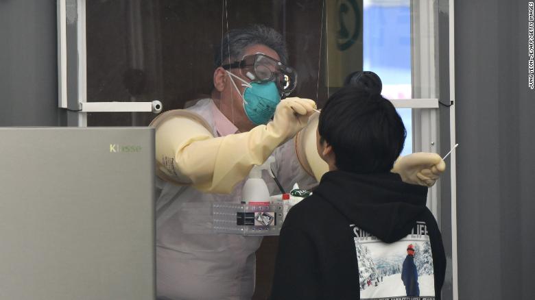 A medical staff member in a booth takes samples from a visitor for the Covid-19 coronavirus test at a walk-thru testing station set up at Jamsil Sports Complex in Seoul on April 3, 2020. 