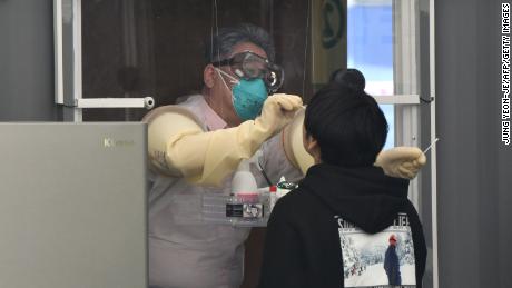 A medical staff member in a booth takes samples from a visitor for the Covid-19 coronavirus test at a walk-thru testing station set up at Jamsil Sports Complex in Seoul on April 3, 2020. 