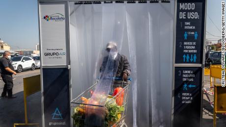 A person wearing a protective mask pushes a grocery cart through a decontamination chamber at the La Vega Central fruit and vegetable market in Santiago, Chile.