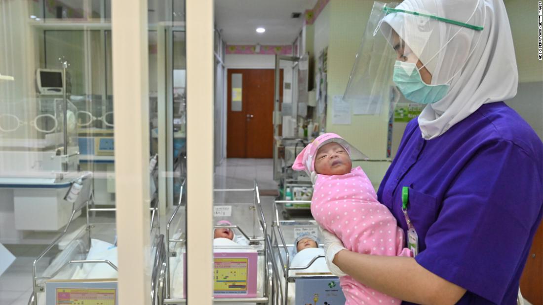 A nurse holds a newborn baby, wearing a face shield as a protective measure, at a maternity facility in Jakarta, Indonesia.