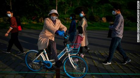 A woman wearing a facemask takes a rest on a bicycle along the East Lake in Wuhan, in China&#39;s central Hubei province on April 12, 2020. (Photo by Hector RETAMAL / AFP) (Photo by HECTOR RETAMAL/AFP via Getty Images)