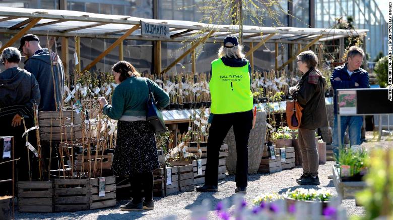 An employee wears a vest reading &quot;Keep distance. Stop Covid-19&quot; as customers look at plants at the Slottstradgarden Ulriksdal garden centre in the Ulriksdal Palace park in Stockholm on April 21.