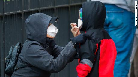 A woman adjusts her child&#39;s mask as they wait in line to be screened for Covid-19 in New York. 