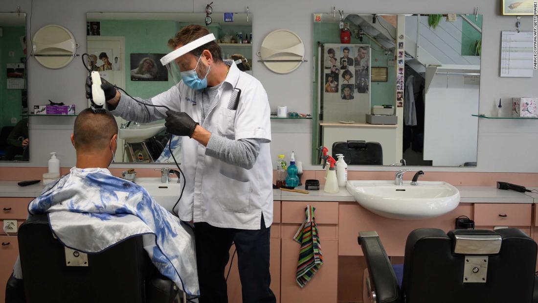 A barber wears protective equipment as he cuts a customer&#39;s hair in Lausanne, Switzerland.