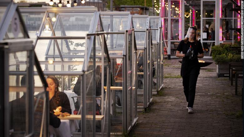 A waitress wearing a protective face shield arrives to serve wine to friends having dinner in a so-called quarantine greenhouses in Amsterdam, on May 5, 2020 as the country fights against the spread of the COVID-19, the novel coronavirus. 