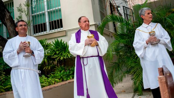 From left, minister Ismael Fletcher, Monsignor Jose Emilio Cummins and minister Eva Pilar Garcia wait in front of a parish in San Juan, Puerto Rico, during a drive-thru communion on March 21.