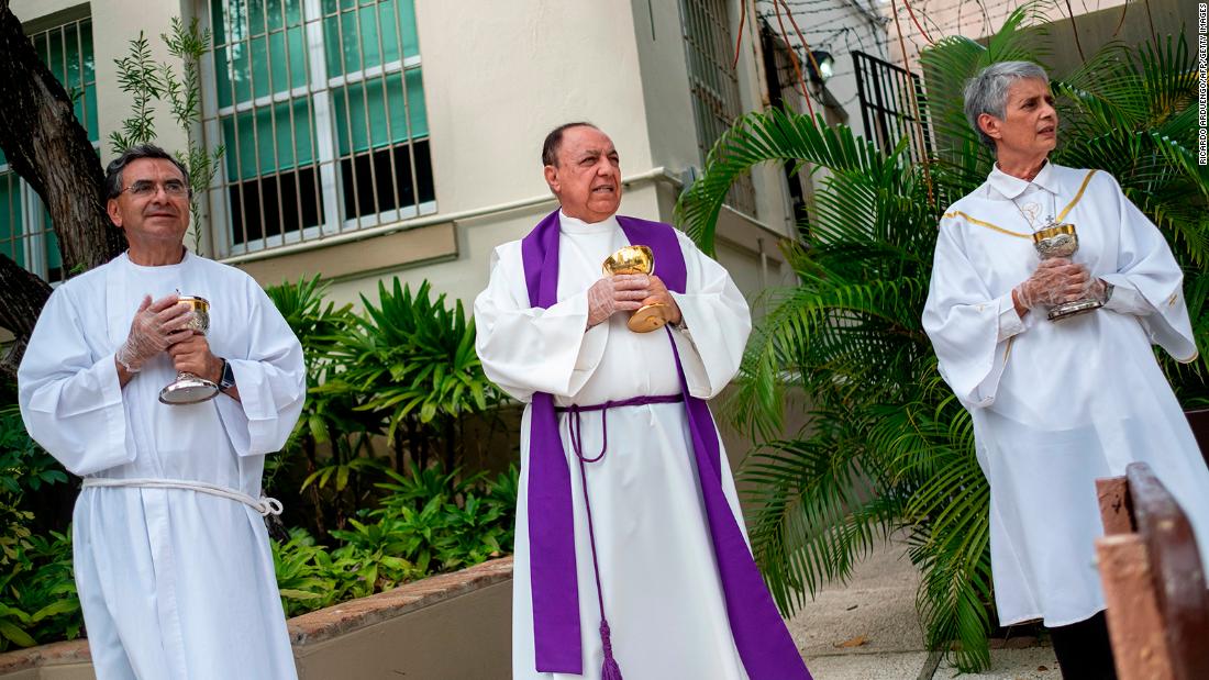 From left, minister Ismael Fletcher, Monsignor Jose Emilio Cummins and minister Eva Pilar Garcia wait in front of a parish in San Juan, Puerto Rico, during a drive-thru communion on March 21.