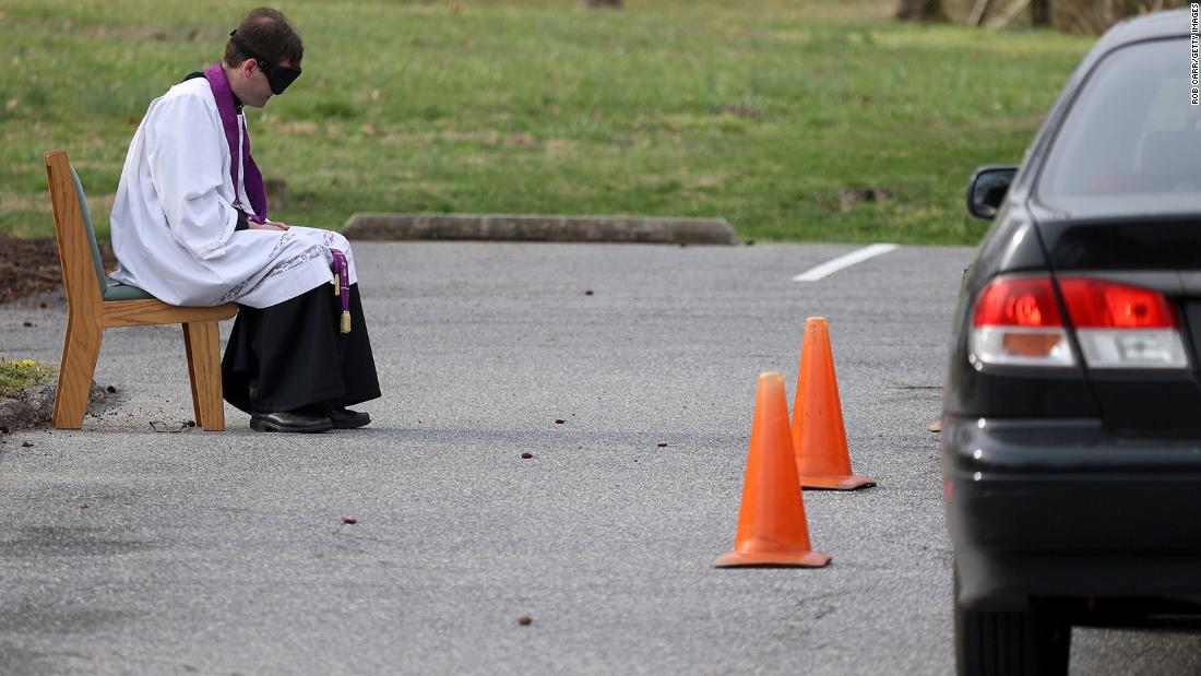 The Rev. Scott Holmer offers a drive-thru confessional March 20 in the parking lot of St. Edward the Confessor Catholic Church in Bowie, Maryland. Holmer sits 6 feet away from cars as people pull up to talk to him.