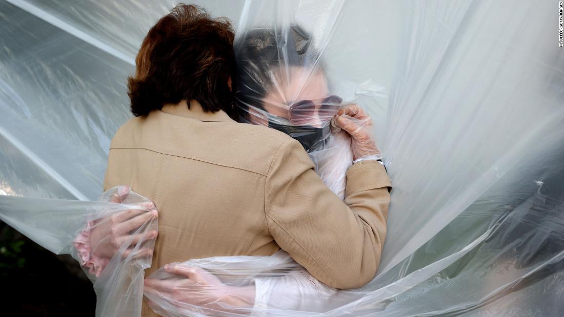 Olivia Grant, right, hugs her grandmother, Mary Grace Sileo, through a plastic drop cloth that was hung up on a homemade clothesline in Wantagh, New York.