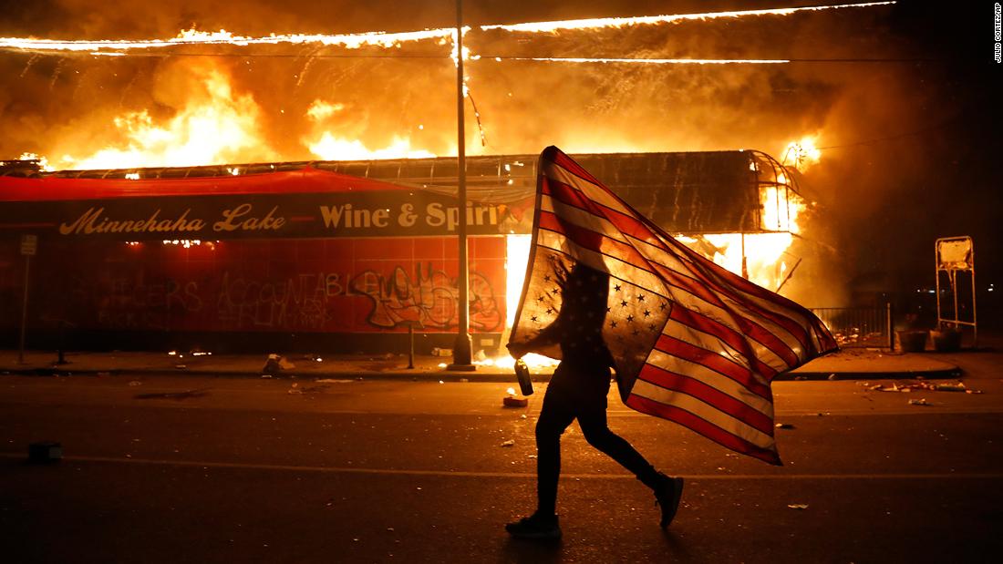 A protester carries an American flag upside down next to a burning building in Minneapolis on May 28.