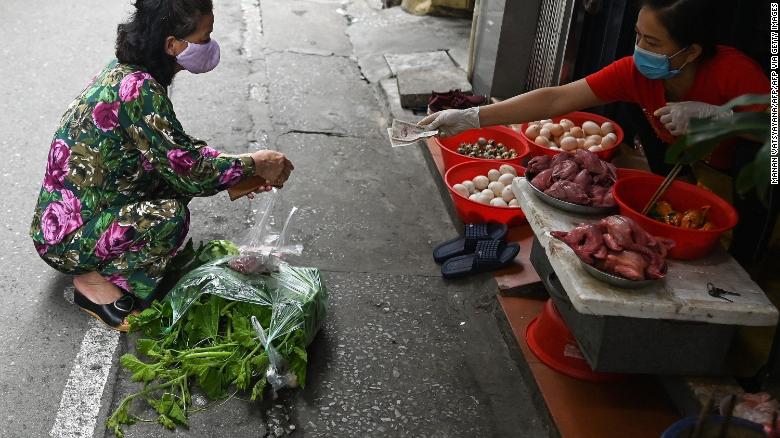 A woman practises social distancing while shopping for groceries from behind a line at a wet market in Hanoi.