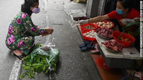 Una mujer practica el distanciamiento social mientras hace compras detrás de una línea en un mercado húmedo en Hanoi.