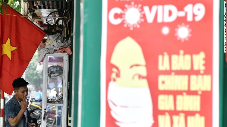 A propaganda poster on preventing the spread of the coronavirus is seen on a wall as a man smokes a cigarette along a street in Hanoi.