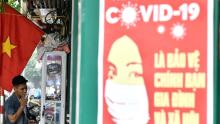 Un afiș de propagandă pentru prevenirea răspândirii coronavirusului este vizibil pe un perete, deoarece un bărbat fumează o țigară pe o stradă din Hanoi.