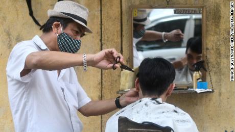 Un peluquero en la carretera con una máscara facial le corta el pelo a un cliente en Hanoi.