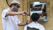 Un frizer pe marginea drumului care poartă o mască facial dă o tunsoare unui client din Hanoi.