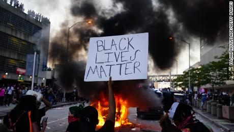     Un hombre tiene un cartel de Black Lives Matter en la mano mientras un auto de policía se quema durante una protesta en Atlanta el viernes.