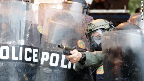 A policeman shoots rubber bullets at protesters throwing rocks and water bottles during a demonstration in Miami.