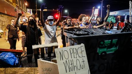 Protesters raise their hands beside a fence intended to block potential police advances at a memorial for George Floyd where he died outside Cup Foods on East 38th Street and Chicago Avenue, Monday, June 1, 2020, in Minneapolis. 