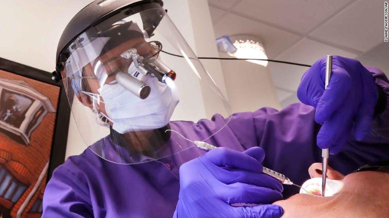 Dentist Dr. Kathleen Saturay wears additional protective equipment, including a face shield and disposable mask over a respirator mask, as she works with a patient in Seattle.