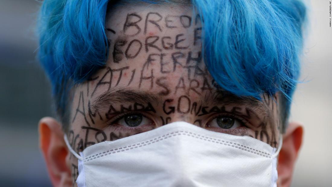 A man attending a demonstration in Berlin, with the names of victims of police violence written on his face.