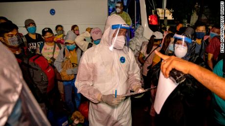 Workers in protective suits are seen as Filipinos out of work and stranded due to the coronavirus pandemic queue to take a free bus ride home to their province on May 29, 2020 in Paranaque, Metro Manila.