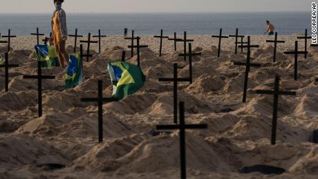 A woman walks amid symbolic graves on Rio de Janeiro&#39;s Copacabana beach. They were dug by activists protesting the government&#39;s handling of the Covid-19 pandemic.