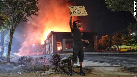 A person holds a sign as a Wendy&#39;s restaurant burns Saturday in Atlanta